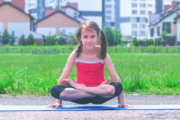 Mavi minder üzerinde yoga yapan genç ve çekici bir kız bacak bacak bacak üstüne atarak kol dengesi egzersizi, duruş şekli, Tolasana, Utpluthi Poz, tam boy.