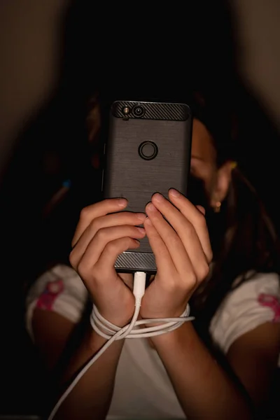 Young child girl playing smartphones during night time. She is chatting with her friend. Using phone in low light is impact to eyes. Health and gadget addiction concept. Vertical image.