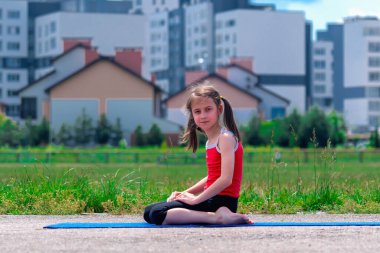 Spor kıyafeti giyen genç bir kız antrenman için çimlerin üzerinde oturuyor.