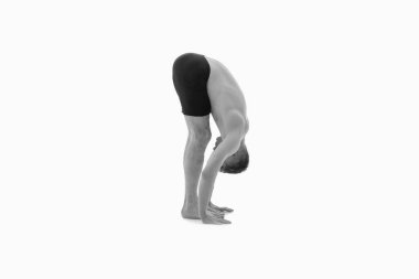 Uttanasana (Standing Forward Bend), Ashtanga yoga. Spor kıyafetleri giyen bir adamın beyaz arka planda yoga egzersizi yapmasını. Siyah ve beyaz resim.