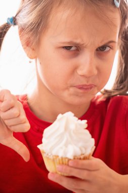 Genç ve güzel bir kızın portresi, parmağıyla pastayı işaret ediyor ve baş parmağını, besleyici olmayan ve sağlıksız yiyeceklerin sembolü olarak gösteriyor. Dikey resim.