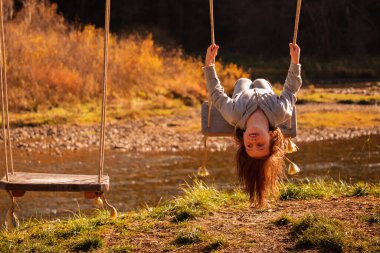Çocukların uçabilme hayalleri. Güzel genç kız salıncakta baş aşağı oturuyor. Mutlu çocukluk ve özgürlük kavramı. Yatay resim.