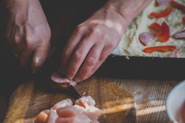 Evde, bir kadın pizza malzemelerini kendi elleriyle hazırlar. Sosisi kesiyor. Boşluğu kopyala.