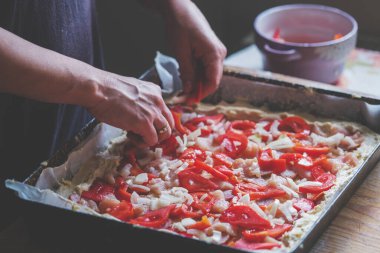 Şefin elleri pizza, domates dilimi, maydanoz ve fesleğen ekliyor. Lezzetli pizza hazırlığı.