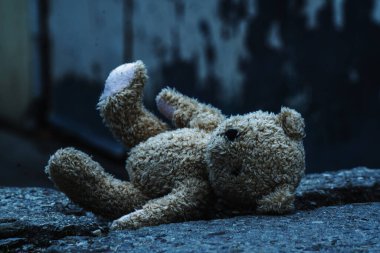 Kavramsal görüntü: kayıp çocukluk, acı, umutsuz ve çökmüş hayat konsepti. Oyuncak ayı kirli asfaltta yatıyor.  