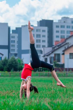Şehirde çimlerin üzerinde egzersiz yapan formda bir kız. Sağlıklı genç bayan sporcu spor yapıyor. Sporcu kız dışarıda spor kıyafeti giyerek antrenman yapıyor. Dikey resim.