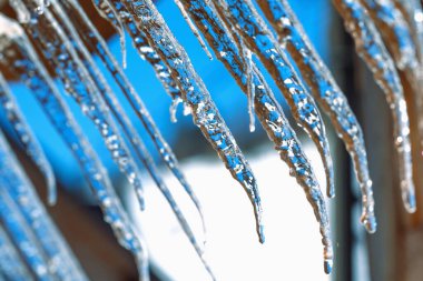 Açık mavi gökyüzüne karşı buz saçağı. Erimiş kar damlası düşer. - Yakın çekim. Kışın sonu ya da baharın başlangıcı hakkında bir resim. 