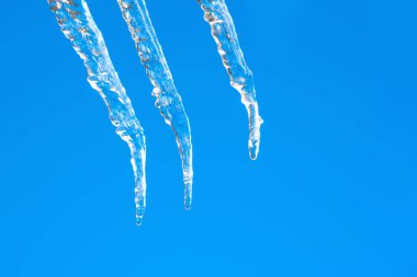 Açık mavi gökyüzüne karşı buz saçağı. Erimiş kar damlası düşer. - Yakın çekim. Kışın sonuyla ya da baharın başlangıcıyla ilgili bir resim. Buzlar çözülsün. Makro görüntü. Boşluğu kopyala.