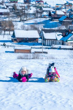 Karlı dağ kasabasında karların üzerinde uzanan tepe, kış dağlarına bakıyor. Kış aile tatili, Noel kutlaması ve kış tatili 