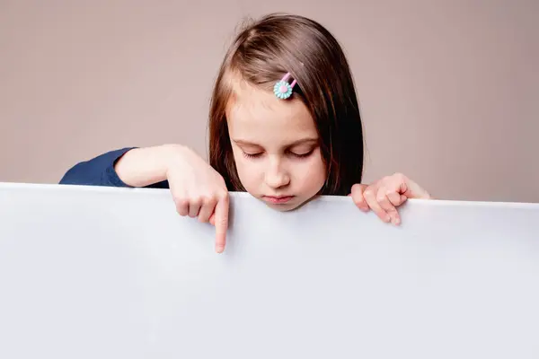 Beautiful young girl pointing with finger on white blank banner or empty copy space advertisement board. Copy space for text or design. Horizontal image.