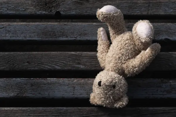Conceptual image: lost childhood, loneliness, pain and depression. Close up dirty toy Teddy bear lying down outdoors on grey asphalt. Broken toys, broken life. Copy space for text or design.