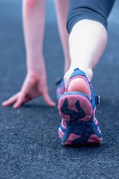 Athlete young girl in running start pose. Selective focus on feet running on road closeup on shoe.  Vertical image.