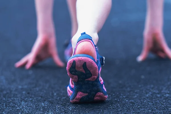 Athlete girl in running start pose. Selective focus on feet running on road closeup on shoe.
