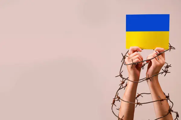 Hands in barbed wire holding flag of Ukraine as symbol of the struggle for freedom and democracy of the Ukrainian people, russia\'s war and aggression against Ukraine. Copy space.
