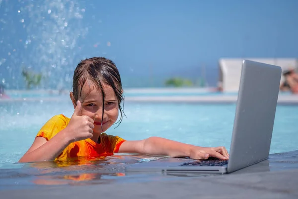 Distance learning concept. Portrait of young child girl having a video chat through laptop on the sea beach.