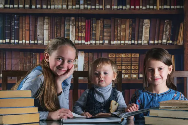 Child development and early learning. Portrait of happy young scientists studying and reading books  in the library against old books background.