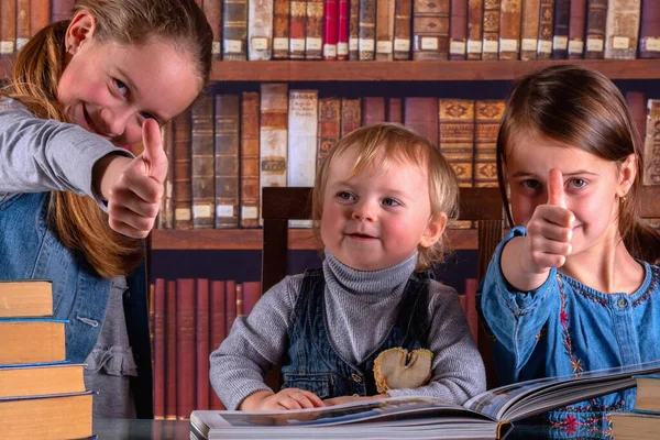 Conceptual image: child development and early learning. Young scientists showing thumbs up sign, studying and reading books  in the library. Humorous photo.