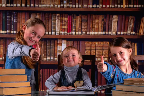 Conceptual image: child development and early learning. Young scientists showing thumbs up sign, studying and reading books  in the library. Horizontal image.