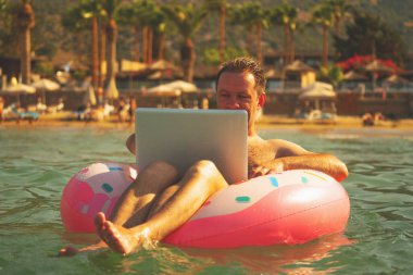 Uzaktan kumandayla ilgili rüyalar. Okyanusta ya da denizde dizüstü bilgisayarla yüzen bir iş adamı. Mesafeli çalışan mutlu iş adamının portresi ve suda şişme bir tekerleğin üzerinde dinleniyor.. 