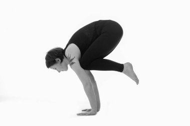 Bakasana (Crane Poose), Ashtanga yoga tarafı manzaralı spor giyimli kadın beyaz arka planda yoga yaparken görülüyor. Siyah ve beyaz resim.