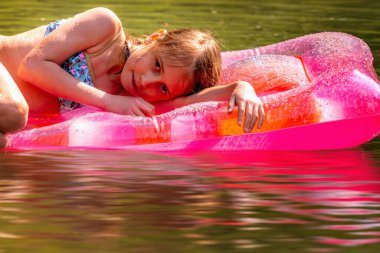 Nehirde pembe şişme bir yatakta yüzen göz kamaştırıcı genç kızın portresini yakından çek. Yaz tatili, tatil, dinlenme konsepti. Yatay resim.