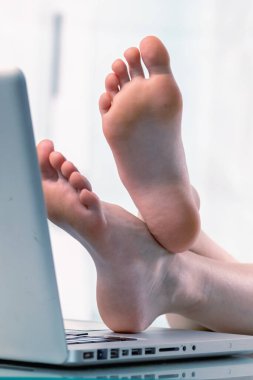 Bugün çalışmak için havamda değilim. Genç iş kızı dizüstü bilgisayarın başına çıplak ayakla geçti. Ofiste çalışmak istemiyor. Dikey resim.