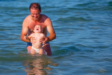 Çocukların mutluluğu, güvenliği, bağlılığı, psikolojik sağlık konsepti. Okyanusta oynayan çocuklu mutlu bir baba. Metin veya tasarım için boşluk kopyala.