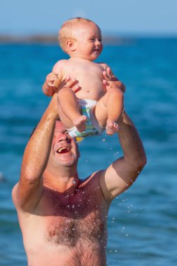 Baba, bebekle birlikte denizde yüzüyor. Doğa, seyahat, okyanusta oynayan mutlu baba ve çocuk. Dikey resim.