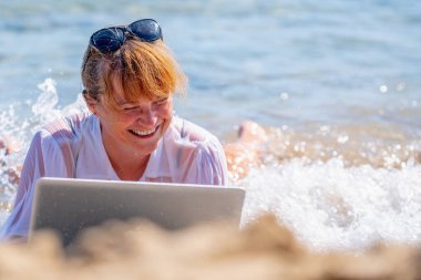 Portrait of very happy businesswoman is happy to work online with laptop on the beach of sea or ocean.  Horizontal image. clipart