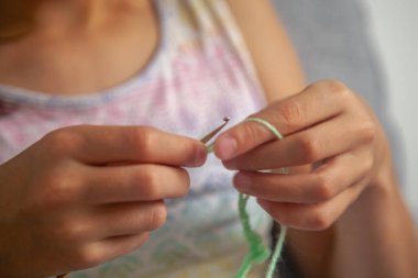 Tığ işi süreci. El ve örgü ipliği kullanan genç bir kızın portresi, el yapımı tığ işi, evde dinlenmek için hobi. Parmaklarına odaklan. Yatay resim.