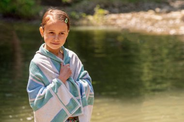 Deniz sahilinde, bitkilerin koyu yeşil arka planına karşı havluyla kaplanmış güzel bir kız. Yaz tatili ve tatil konsepti. Metin veya tasarım için boşluk kopyala
