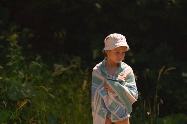 Deniz sahilinde, bitkilerin koyu yeşil arka planına karşı havluyla kaplanmış güzel bir kız. Boşluğu kopyala.