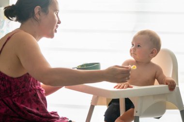 Evdeki mutfakta bebeğini besleyen esmer bir annenin portresi.