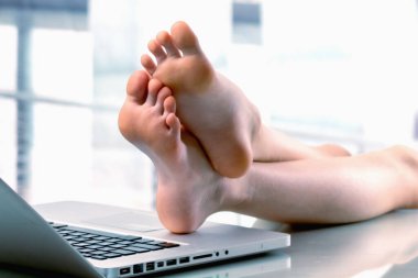 Bugün çalışmak için havamda değilim. Neşeli genç iş kızı dizüstü bilgisayara çıplak ayaklarını koydu, çalışmak istemiyor..