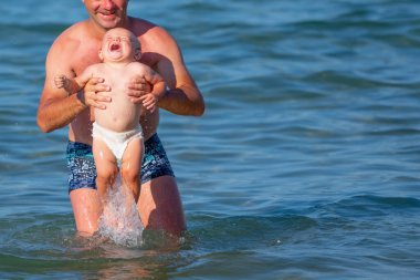 Çocukların mutluluğu, güvenliği, bağlılığı, psikolojik sağlık konsepti. Okyanusta oynayan mutlu baba ve çocuk. Metin veya tasarım için boşluk kopyala.
