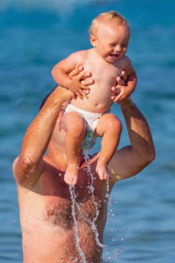 Baba, bebekle birlikte denizde yüzüyor. Doğa, seyahat, okyanusta oynayan mutlu baba ve çocuk. Metin veya tasarım için boşluk kopyala. Yatay resim.