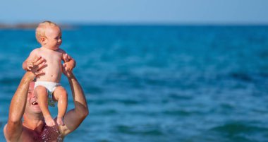 Baba, bebekle birlikte denizde yüzüyor. Doğa, seyahat, okyanusta oynayan mutlu baba ve çocuk. Metin veya tasarım için boşluk kopyala. Yatay resim.