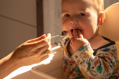 Otururken yulaf lapasıyla beslenen küçük, neşeli bir çocuğun portresi. Organik bebek maması konsepti.
