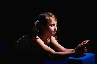 Güzel genç kız başaşağı eğik bacak ve köpük küplere bacak tutarak yoga pratik yaparken tatmin gülümseme ile, paspas karşı siyah arka plan egzersiz. 