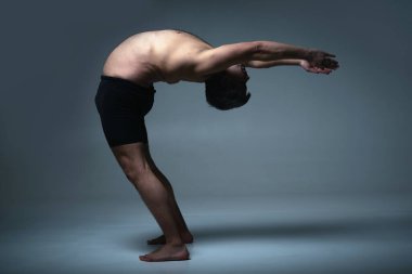 Ashtanga yogası. Spor giysili bir adamın karanlık arka planda yoga yaparken görüntüsü..