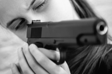 Kavramsal imaj: silah sahibi olmak ve çocuk suçu. Genç bir kız silah doğrultuyor. Yatay siyah beyaz resim.