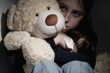 Kavramsal fotoğraf: kayıp çocukluk. Yalnız ve üzgün genç kız ağlıyor ve tek arkadaşı olan oyuncak ayıya sarılıyor.. 