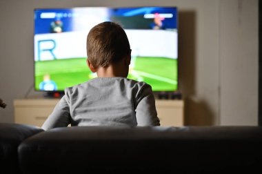 Çocuk kanepede oturup TV 'de futbol izliyor.