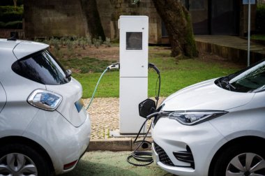 Şehirdeki bir şarj istasyonunda elektrikli bir araç. Şarj kablosundaki beyaz e-araba. Elektrikli araba çevreye duyarlı aracın şarj edildiği taraftan gösteriliyor..