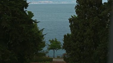 Perdeleri olan kırsal bir pencere, Akdeniz 'in sakin, yeşil, açık hava manzarasını ortaya çıkarmak için açık, loş, loş bir oturma odasında. 4K stok video SlowMo