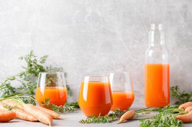Carrot juice in a glass and bottle and fresh carrots with leaves