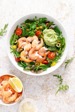 Shrimp and leafy vegetables salad with tomato, bell pepper, olive and avocado sauce. Top view