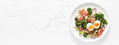 Easter egg salad with prosciutto and broccolini on white background, top view. Easter salad with boiled egg