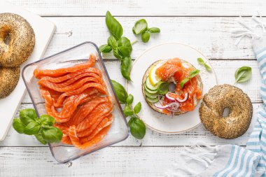 Salmon sandwiches with bagel, salted fish, fresh cucumber, onion and basil on white background, top view. Healthy breakfast with salmon toasts