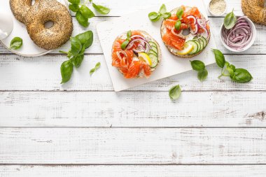 Salmon sandwiches with bagel, salted fish, fresh cucumber, onion and basil on white background, top view. Healthy breakfast with salmon toasts